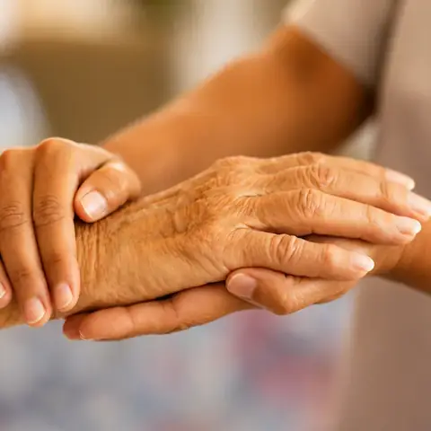 A caregiver gently holding an older person's hands