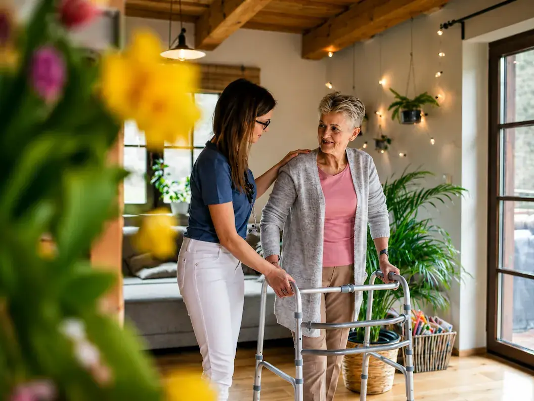 A caregiver helping a senior woman walk safely with her walker at home