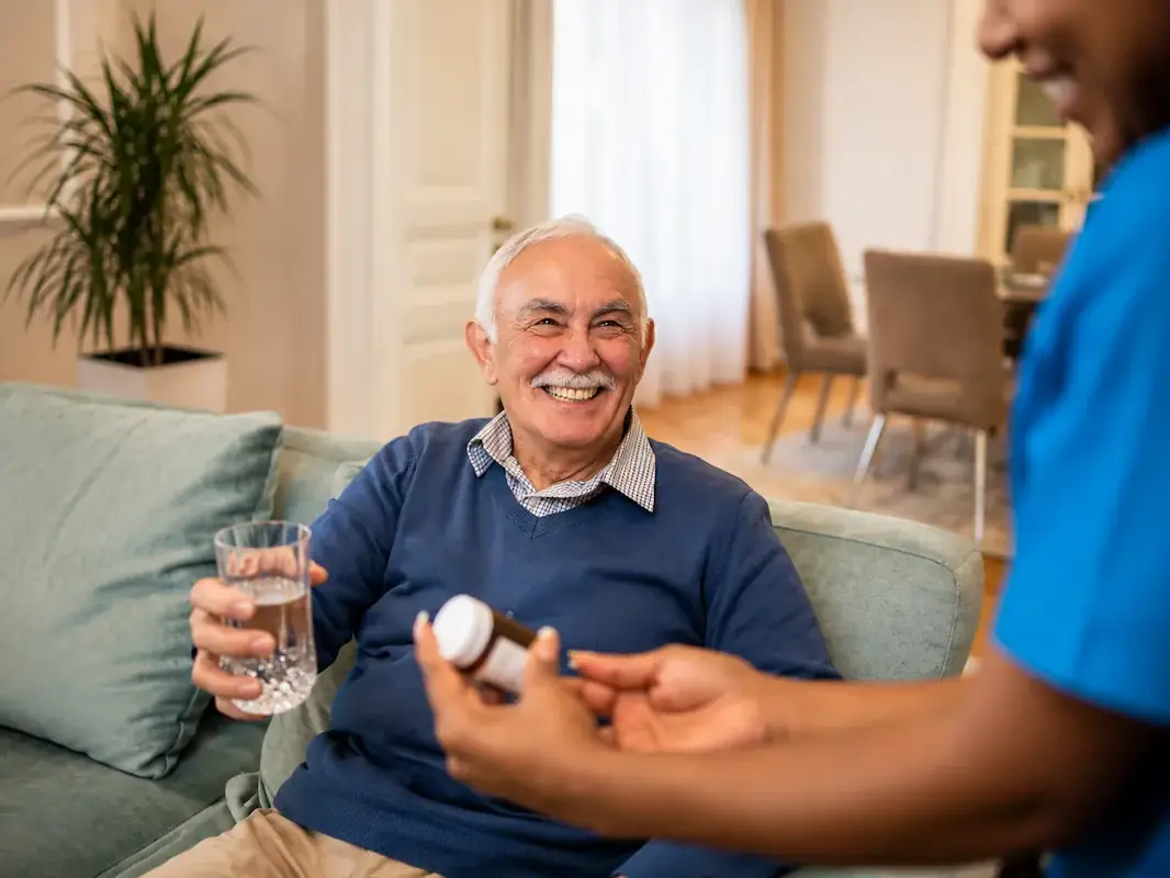 A smiling senior man taking his medication on time with a caregiver's reminder