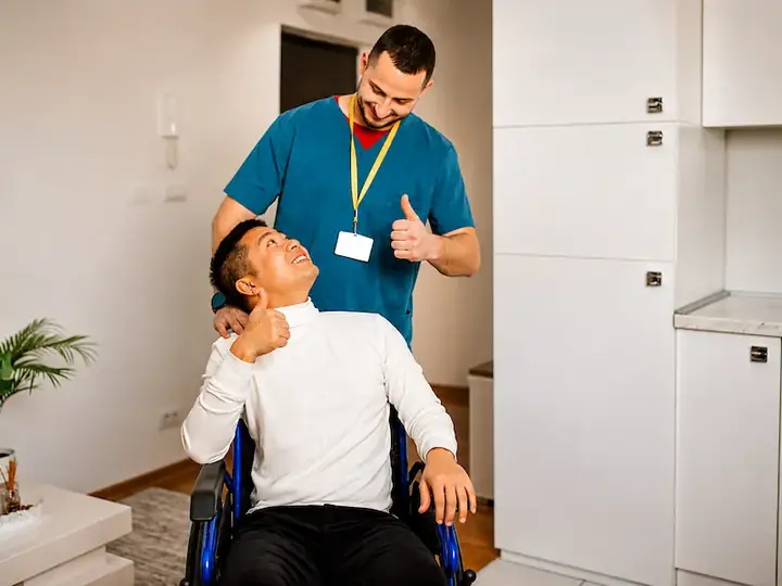 A caregiver encouraging a smiling man who uses a wheelchair